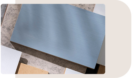 Mehrere Musterplatten verschiedener Materialien und Farben, übereinandergelegt. Im Vordergrund ist eine blaue Platte sichtbar, umgeben von weiteren Platten in Grau-, Beige- und Weißtönen. Die Oberfläche der Platten weist unterschiedliche Texturen auf