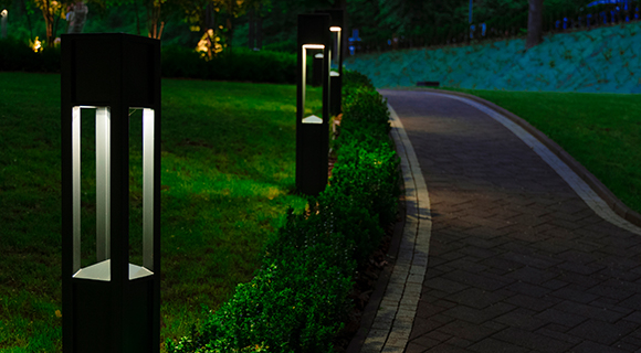Beleuchteter Gartenweg mit modernen Pollerleuchten entlang einer gepflegten Hecke in der Abenddämmerung.