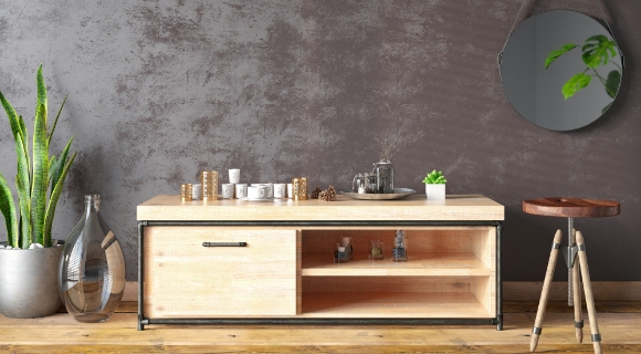 niedrige Kommode in hellem braun, daneben ein Hocker, eine Pflanze und ein Spiegel an der Wand