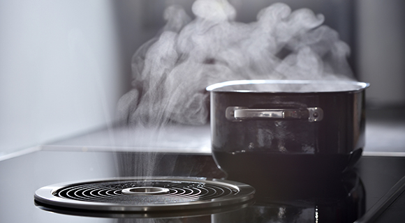 Moderne Küche mit Topf und aufsteigendem Dampf über einem Kochfeld mit Muldenlüfter.