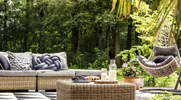Rattan-Gartenm&ouml;bel mit Sofa, Beistelltisch und H&auml;ngesessel auf einer Terrasse im Gr&uuml;nen.