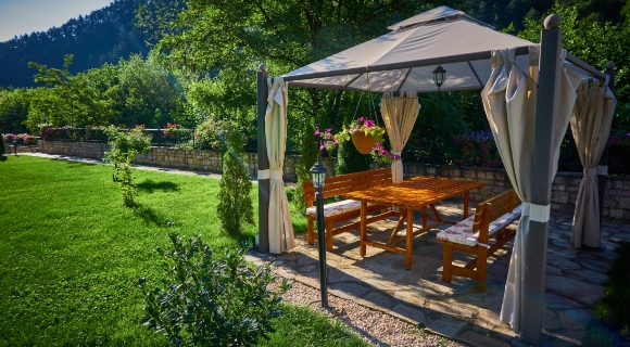 Unter einem Pavillon steht ein Gartentisch mit zwei Gartenb&auml;nken und Sitzpolstern.