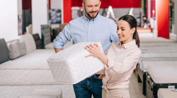 Kundin lässt sich von einem Berater im Fachgeschäft den Aufbau eines Matratzenkerns erklären und fühlt das Material