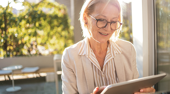 Seniorin mit hellblondem Haar arbeitet oder liest auf einem digitalen Gerät in entspannter Umgebung.