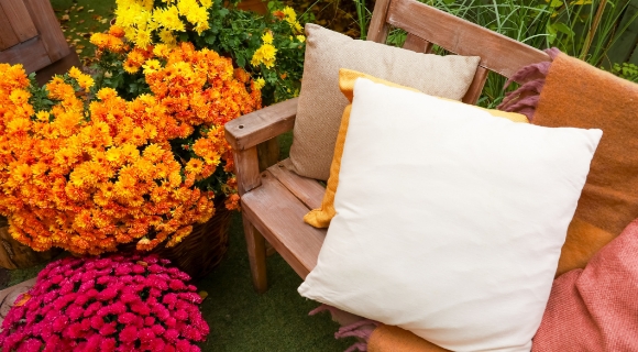Holzbank Sitzkissen vor zwei bl&uuml;henden Blument&ouml;pfen im Garten.