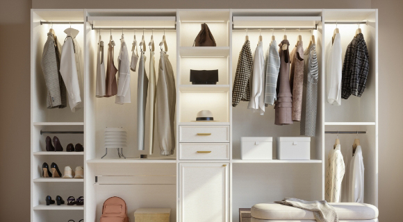 Offener, heller Kleiderschrank mit mehreren Fächern, Kleiderstangen, Schubladen und Beleuchtung, gefüllt mit Kleidung, Schuhen und Accessoires.