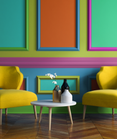 Zwei gelbe Sessel und ein runder Couchtisch mit Dekovasen vor einer bunt gestrichenen Wand mit klassischen Zierleisten