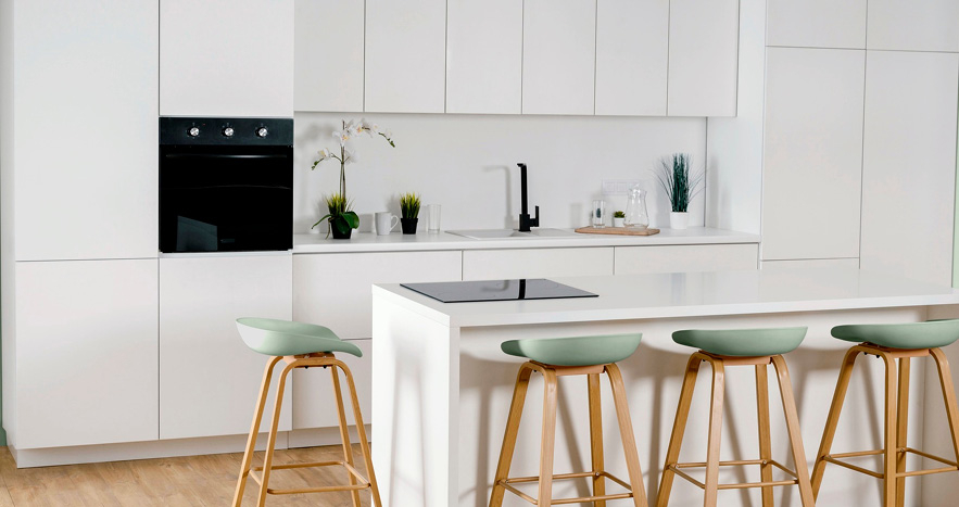 Moderne, minimalistische Küche in Weiß mit Kochinsel und Barhockern. Die Küche verfügt über weiße Schränke, eine integrierte schwarze Backofeneinheit und eine weiße Arbeitsfläche mit schwarzer Armatur. Auf der Kochinsel stehen vier Hocker mit mintgrünen Sitzflächen und Holzbeinen. Kleine Pflanzen und Dekorationsgegenstände verleihen dem Raum eine frische Atmosphäre