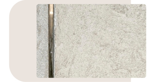 Detailansicht einer Oberfläche in Betonoptik mit einem schmalen Metalleinsatz. Die Textur der Betonoberfläche ist rau und strukturiert, was der Küche einen industriellen Look verleiht
