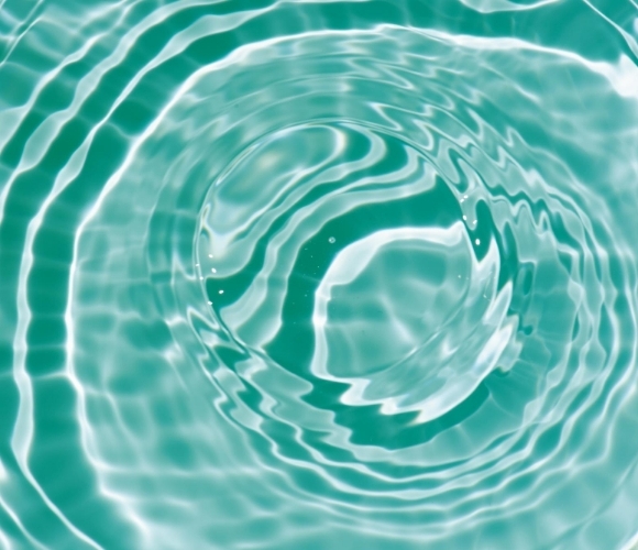T&uuml;rkisfarbenes Wasser mit konzentrischen Wellenringen und Lichtreflexen auf der Oberfl&auml;che.