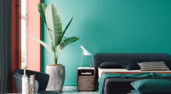 Designbett mit gesteppter Rückenlehne in modernem Schlafzimmer mit farbintensiver Wandgestaltung, großen Pflanzen und kreativer Deckenoptik im Streifenlook