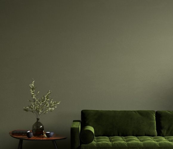 Modern eingerichteter Raum. Die Wand ist grün gestrichen. Vor der Wand steht ein grünes Sofa und daneben ein kleiner Tisch mit dekorativer Deko.