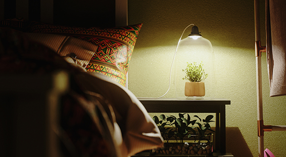 Nachttisch mit beleuchteter Glaslampe und kleinem Pflanzenterrarium neben Bett mit gemustertem Kissen.