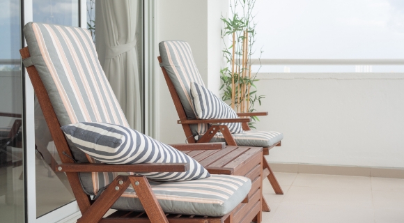 Balkon mit zwei Holzst&uuml;hlen, gestreiften Sitzkissen und kleinem Holztisch  vor gro&szlig;er Fensterfront