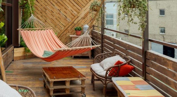 Holzterrasse mit H&auml;ngematte, Sitzm&ouml;beln, niedrigem Tisch aus Paletten und h&auml;ngenden Pflanzen.