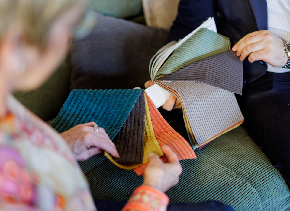 Zwei Personen vergleichen Farb- und Materialmuster f&uuml;r Innenraumgestaltung auf einem Sofa.