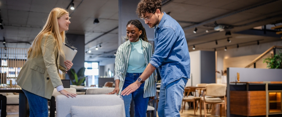 Drei Personen im M&ouml;belgesch&auml;ft betrachten einen gepolsterten Sessel und pr&uuml;fen Sitzfl&auml;che und Armlehnen im Showroom.