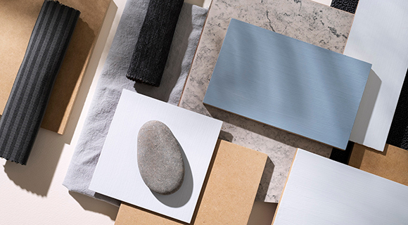 Flach gelegte Auswahl verschiedener Küchenmaterialien und -oberflächen, darunter Holz, Stein, Metall und Stoff, ergänzt durch einen glatten Kieselstein als natürlicher Akzent.