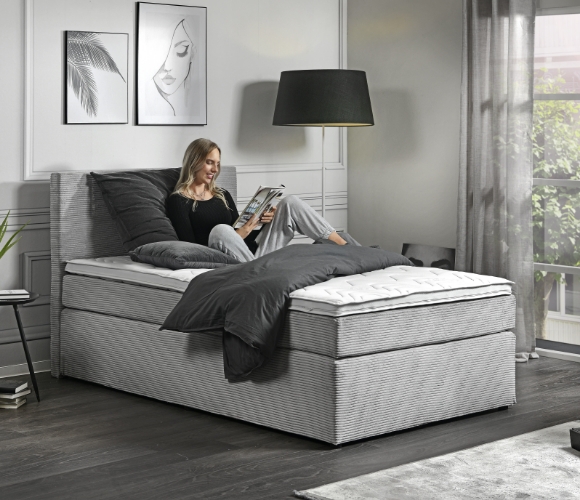 Monochromes Schlafzimmer in Grau mit schwarzen Akzenten. Eine Frau sitzt auf dem Bett und liest.
