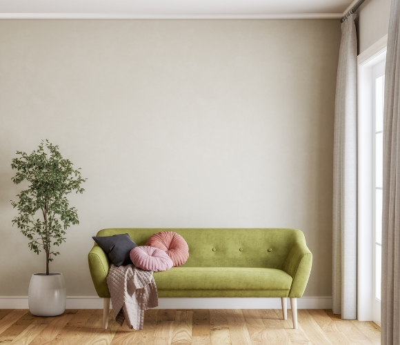Wohnzimmer mit grünem Sofa, Kissen, Decke, Holzfußboden und großem Fenster mit Vorhängen.