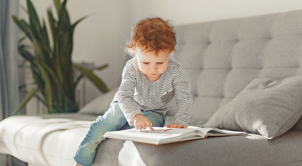 Kleines Kind liest Buch auf einem grauen Schlafsofa