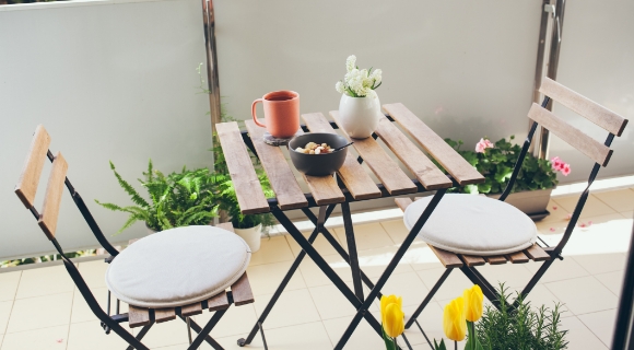 Ein kleiner Balkontisch, mit Bl&uuml;mchen versehen und einer Tasse Kaffee und mit zwei St&uuml;hlen steht auf dem Balkon.