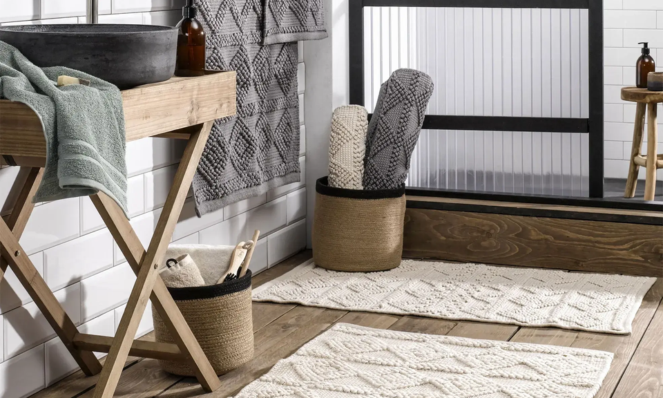 Bad im Ethno-Stil mit Holzdetails, Badteppichen und gewebten Körben vor schwarzer Glasdusche.
