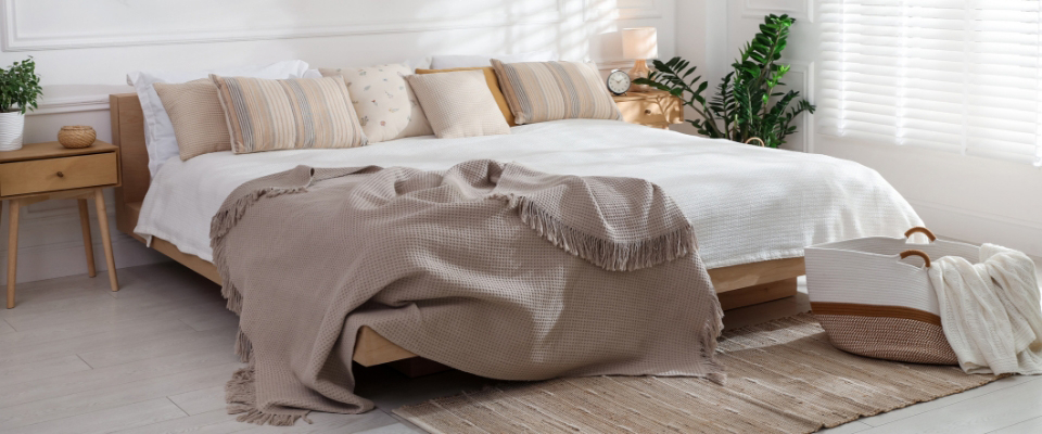 Holz Bett, auf dem mehrere Kissen liegen sowie eine braune Tagesdecke. 