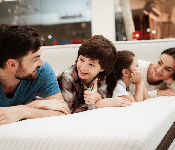 Eine vierköpfige Familie liegt in einem Möbelhaus auf einer Matratze, um diese zu testen.