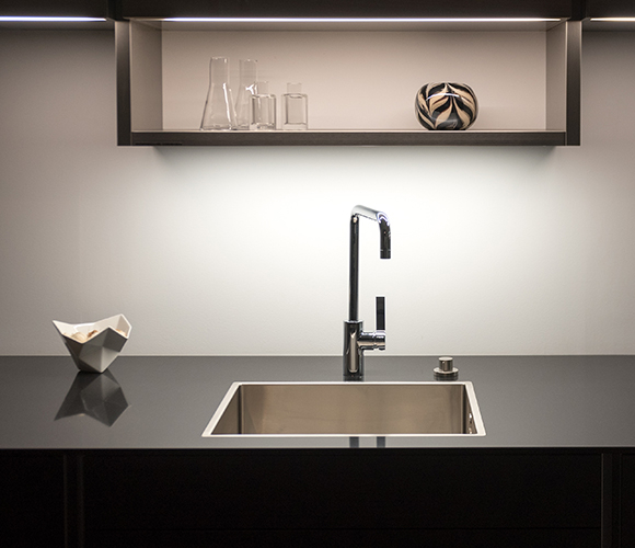 Minimalistische Küchengestaltung mit dunkler Arbeitsfläche, indirekter Beleuchtung und dekorativen Elementen.