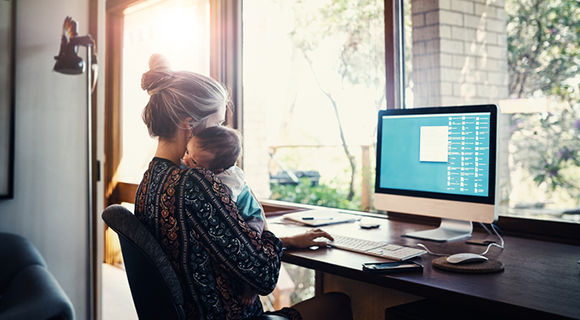 Mutter arbeitet am Computer und hält ihr Kind im Arm.
