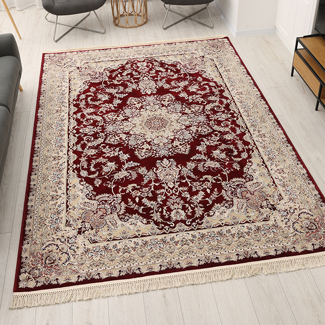 Orientteppich mit klassischen Mustern in Braun und Blau, dekorativ inszeniert auf Fliesenboden mit Kissen und Lesetisch.