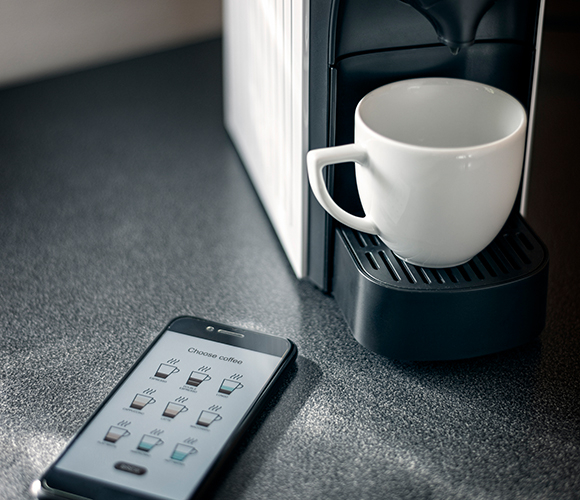 Moderne Kaffeemaschine neben Handy mit App-Steuerung für verschiedene Kaffeevarianten.