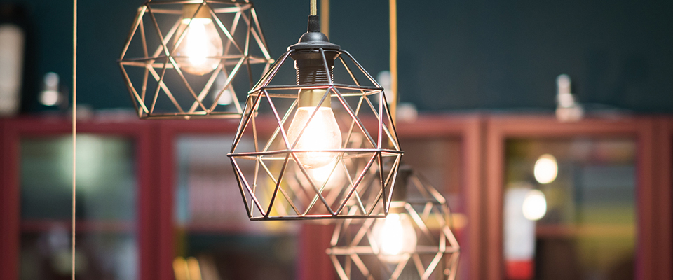 Drei moderne Deckenleuchten mit geometrischem Metallrahmen und warmem Licht über einer Einrichtung im Industrial-Stil.