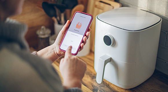 Person nutzt ein Handy, um ein Küchengerät per App zu bedienen.