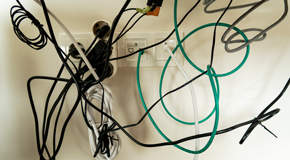 Mehrere ineinander verhedderte Kabel hängen vor einer Steckdosenleiste an der Wand.