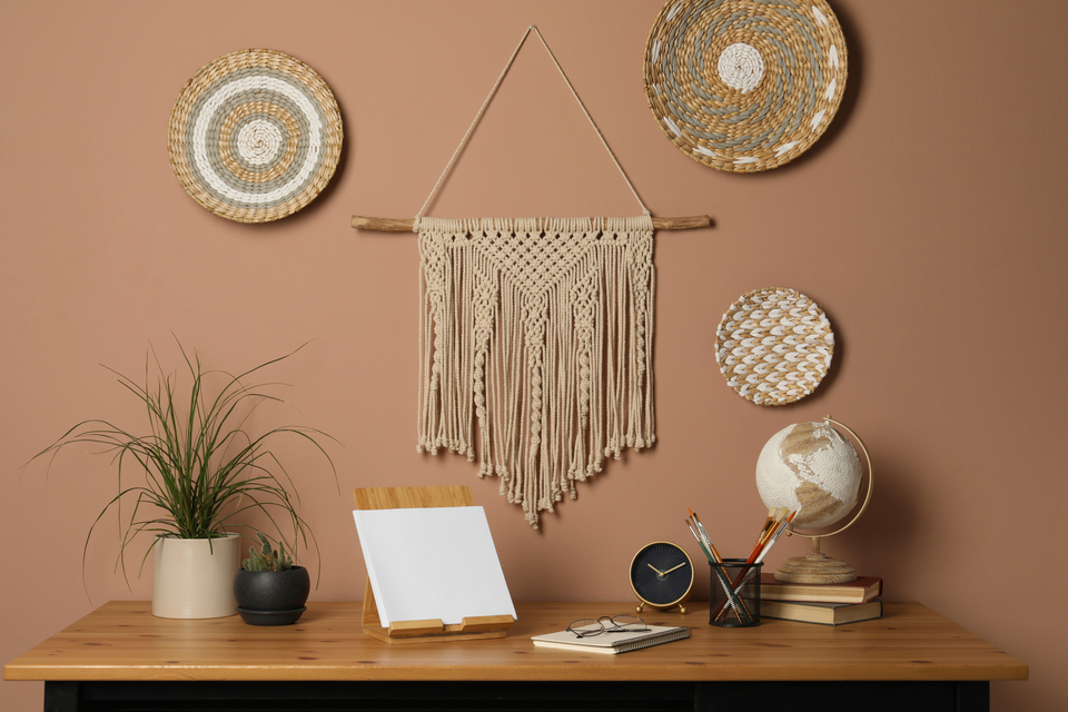 Boho-Arbeitsplatz mit Makramee-Wanddeko, Holztisch, Pflanzen, Globus, Uhr und natürlichen Accessoires