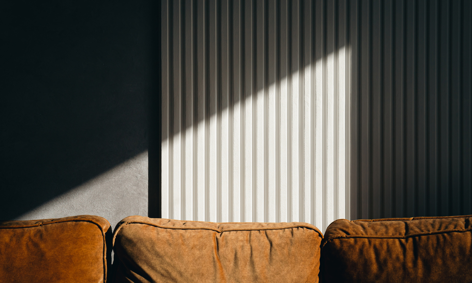 Lichtdurchflutete Szene mit braunem Ledersofa vor geriffelter Wandverkleidung