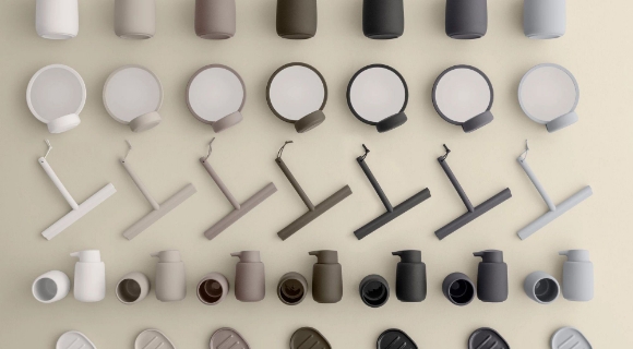 Wandinstallation mit Badezimmer-Accessoires in abgestuften Natur- und Erdtönen von Weiß über Beige, Taupe, Olivgrün und Anthrazit bis Hellgrau.