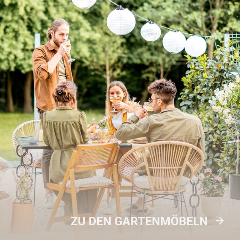 Vier Freunde trinken draußen Tee an einem gedeckten Tisch mit Gartenmöbeln