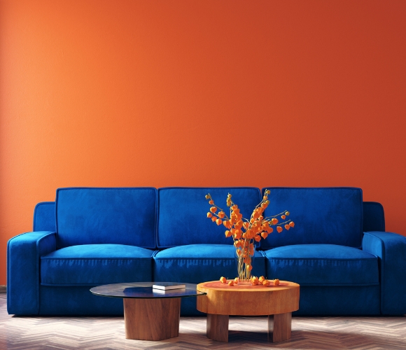 Ein modernes blaues Sofa und ein kleiner Holztisch vor einer orangenen Wand.