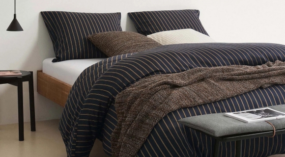 Das Schlafzimmer wurde schlicht eingerichtet. Auf dem Bett liegen Decken und Kissen mit schwarzen Bezügen.
