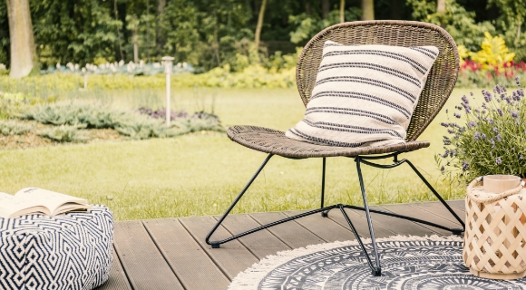 Ein Loungesessel mit einem wei&szlig;-schwarzen Kissen und ein Hocker stehen auf einem Holzdeck im Garten.