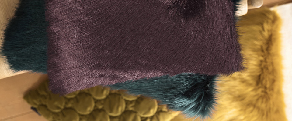 Mehrere flauschige Zierkissen in kräftigen Farben liegen übereinander. Die weichen Materialien sorgen für eine gemütliche und elegante Wohnatmosphäre.