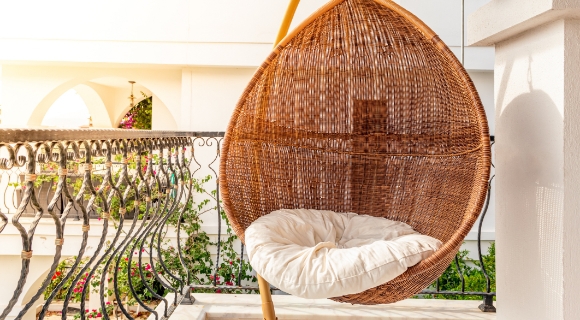 Korb-H&auml;ngesessel mit wei&szlig;em Kissen auf einem Balkon.