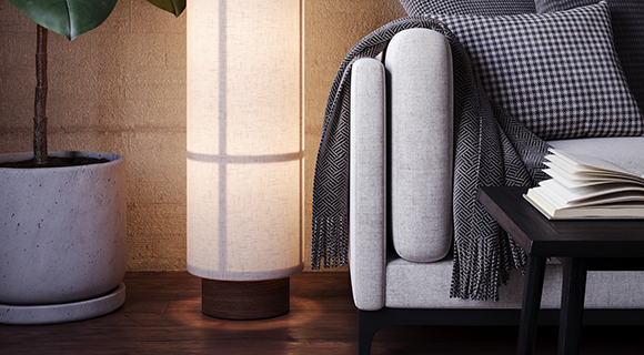 Modernes Wohnzimmer mit grauer Couch, stehender Stofflampe und großer Zimmerpflanze auf Holzboden. 