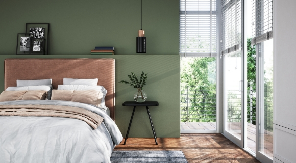 Modern eingerichtetes Schlafzimmer mit gepolstertem Bettkopfteil in Rosé, grüner Wandfarbe und großen Fensterfronten mit Blick ins Grüne