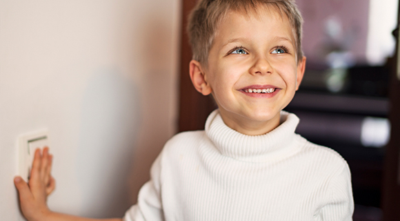Lächelndes Kind im hellen Raum betätigt einen Lichtschalter und freut sich über warmes, angenehmes Licht.