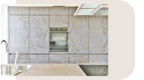 Küche in Betonoptik mit großen, glatten Schrankfronten und einer integrierten Edelstahlspüle. Die Arbeitsfläche besteht aus einer hellen Steinplatte, und ein modernes Kochfeld ist eingebaut. Der Beton-Look der Schränke verleiht der Küche ein industrielles und zugleich elegantes Design.