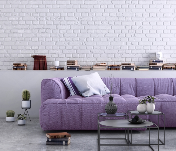 Wohnzimmer mit einem lilafarbenen Sofa, schwarzen Couchtisch, Pflanzen, Vasen und Büchern.